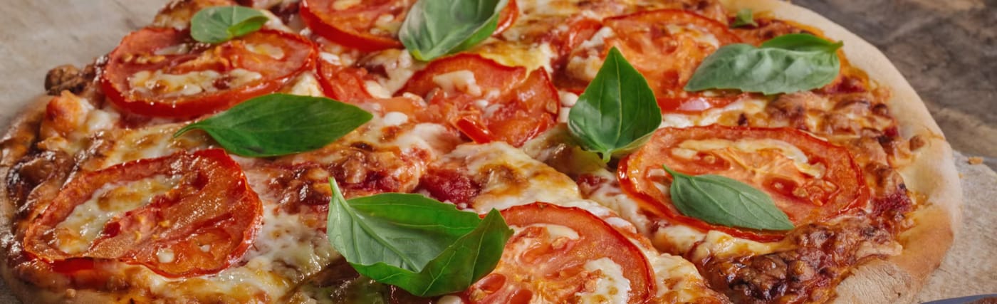 Close-up of a margherita topped with sliced tomatoes, melted mozzarella and fresh basil leaves
